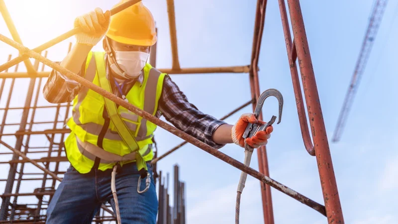 Trabalhador fixa o gancho do talabarte em andaime durante trabalho em altura com EPI conforme a NR-35